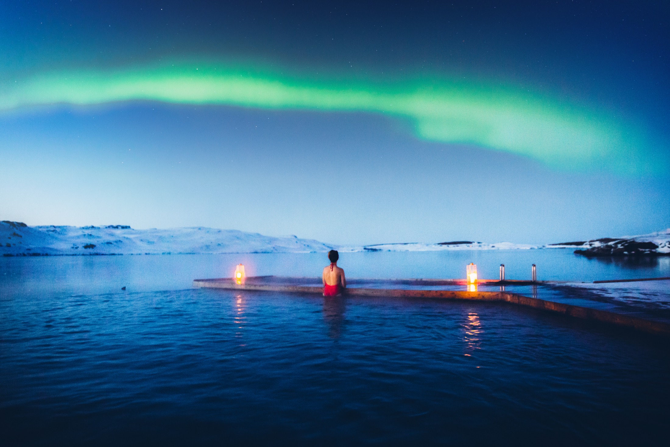 A bather in a geothermal pool at night under the aurora