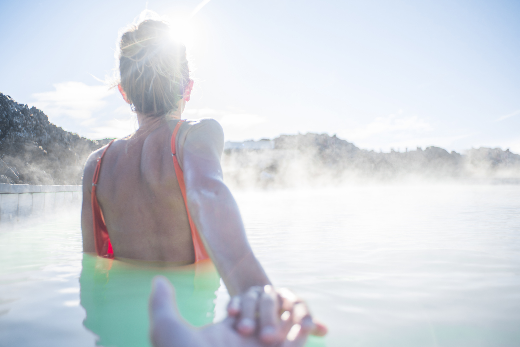 A woman in a steaming geothermal lagoon, reaching forward
